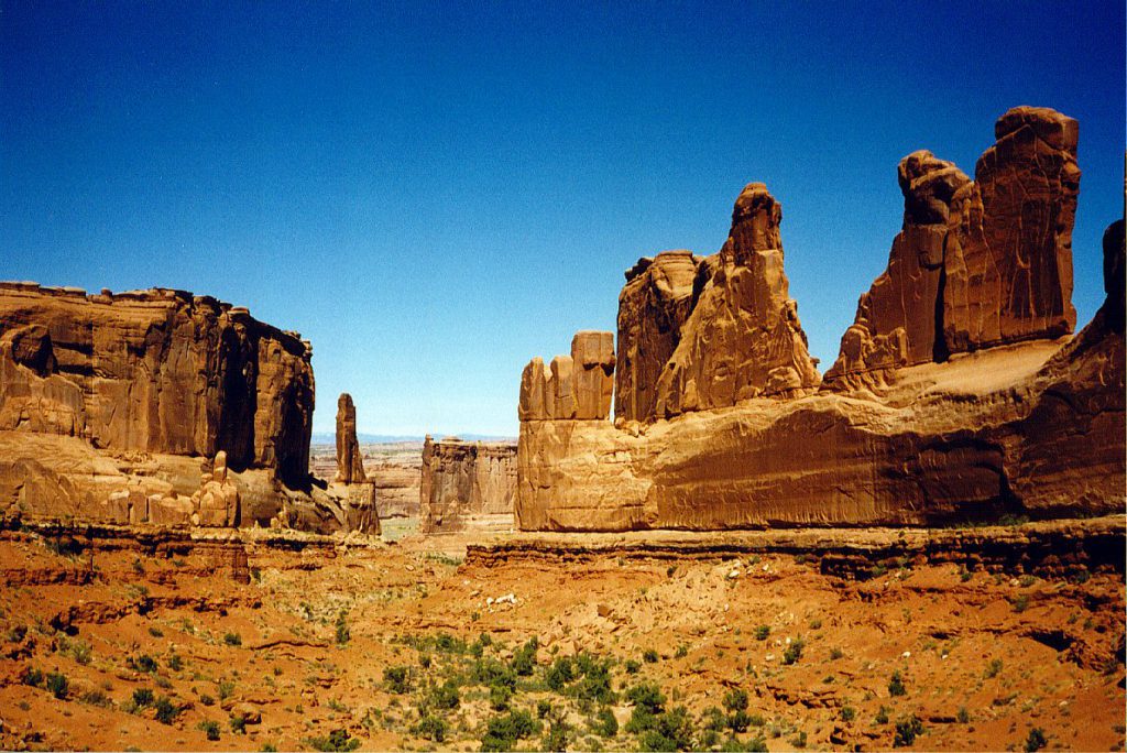 A set of tall thin fins, resembling organ pipes. At some point in the past, there may have been arches here, but they have since collapsed -- yes, arches have finite ages! [The structures in the distance are definitely collapsed arches. Indeed, the road passes through one of the visible gaps]. These fins show areas of darker colouration called 'desert varnish'. This is a familiar site in many locations and is caused by iron and manganese oxides on the surface of the rocks.
