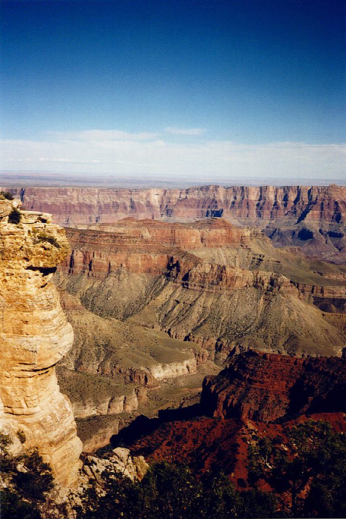 This is a view south-east from the North Rim. You can see a distinct monocline in the South Rim moving from about centre to the left. The Painted Desert is (barely) visible over the lower edge of the monocline. There is a person standing on the edge of the North Rim to the left edge of the photo -- this adds a sense of scale!